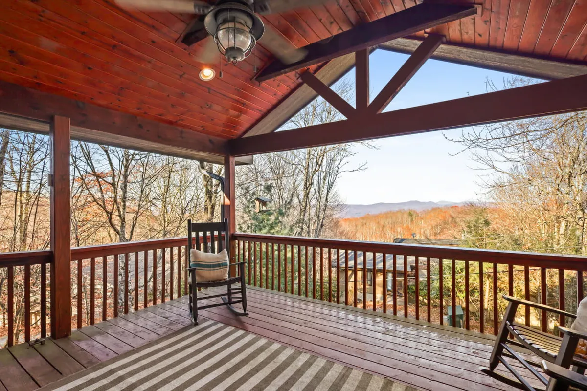 This image features wooden rocking chairs arranged on a deck with a striped rug and a sweeping mountain view beyond. The scene is bathed in natural light, inviting guests to relax and enjoy the tranquil outdoors.