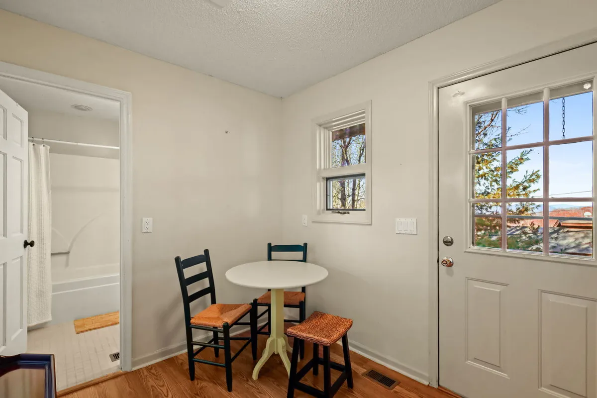 A bright nook with a small round table and two chairs by the window, bathed in natural light. The door with windows opens to the outside, suggesting easy transition from indoor relaxation to outdoor activities.
