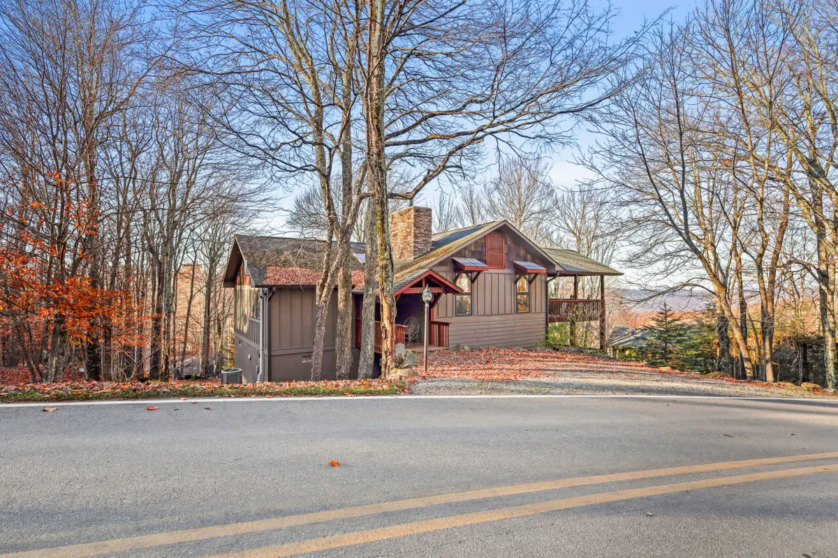 A serene view of the house nestled among vibrant fall foliage and mature trees, with the stone chimney and inviting porch visible. The surrounding open yard offers plenty of space for pets to roam or go on walks with their owners.