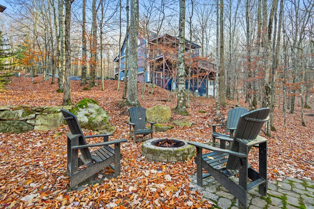A cozy outdoor fire pit area with Adirondack chairs encircled by trees, the house in the background. The space is inviting for gatherings and provides a secure, open area where pets can join their families for relaxation and fun.