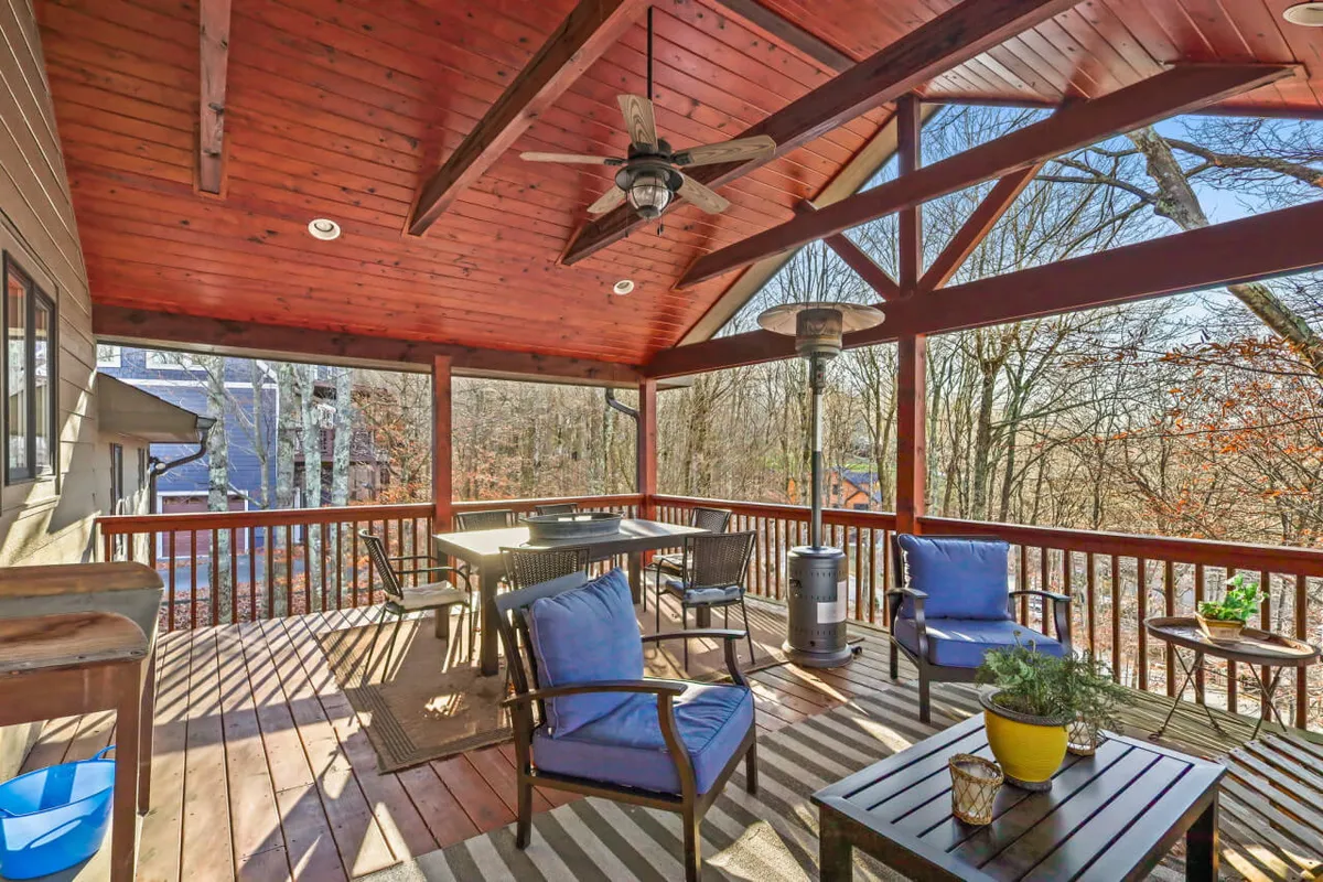 This image features an exterior space with a wooden ceiling, comfortable outdoor seating, a table perfect for gathering, and surrounding trees offering a lush, natural backdrop. The scene exudes a cozy atmosphere ideal for family gatherings after a day of adventure, making it an inviting spot to watch the sunset, enjoy morning coffee, or stargaze at night.