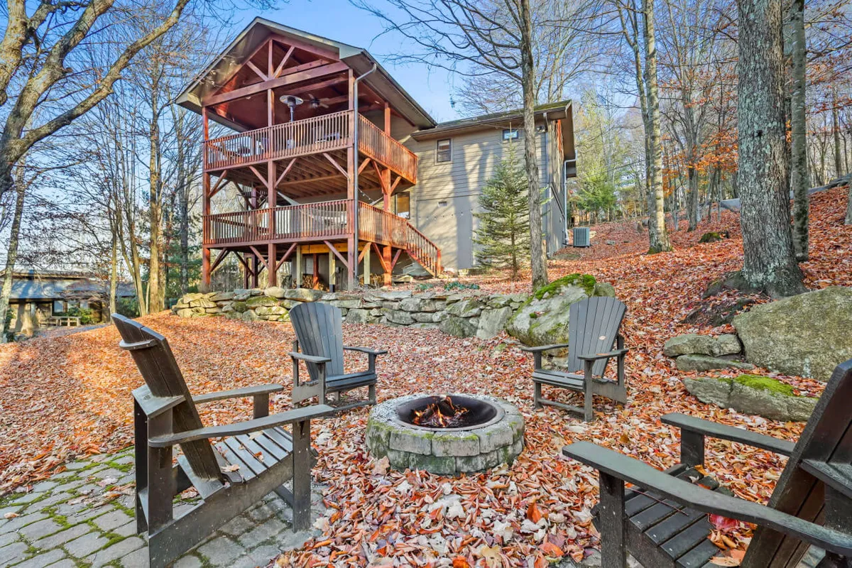 This image captures a large fire pit ringed with chairs in the yard below the deck. The deck and the backdrop of trees and rock formations create a cozy, communal outdoor gathering space.