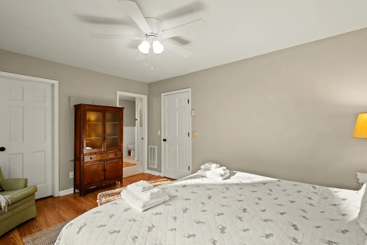 A well-appointed bedroom with a neatly made bed, wooden cabinet, and lamp. The room is softly lit, creating a serene and cozy environment perfect for unwinding and relaxation.