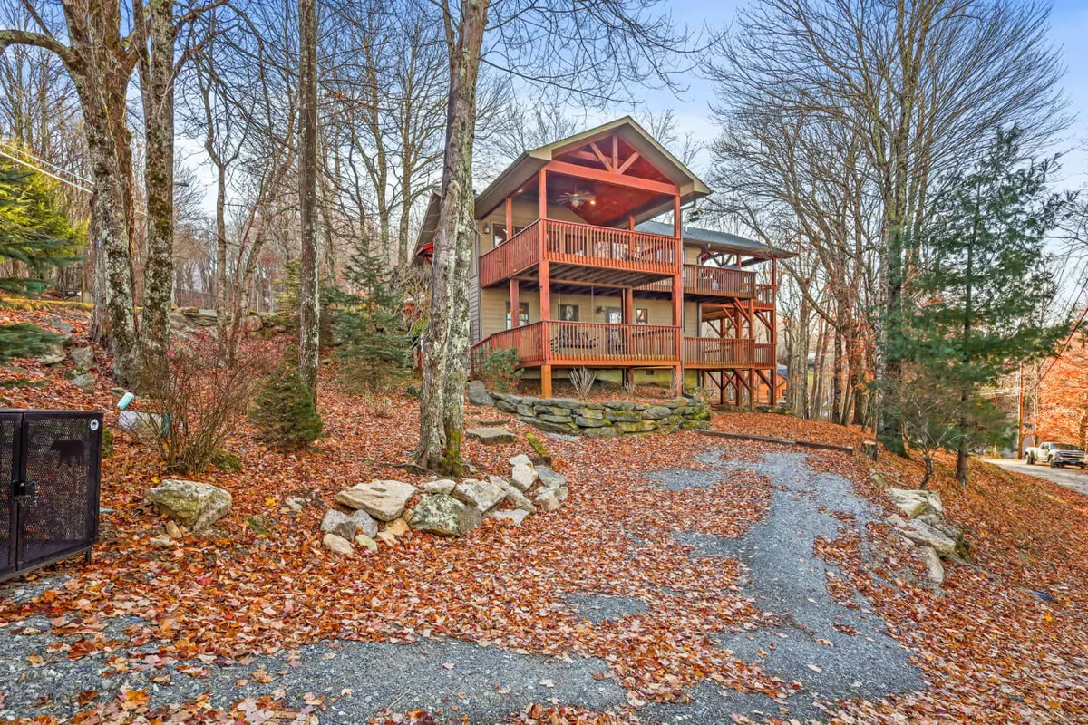 A welcoming wooden deck surrounded by trees, featuring a stone pathway and a view of the house's facade. The setting offers clear access to nature and ample space for outdoor activities, making it ideal for pets to explore or relax.